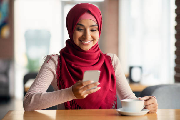 istock Smiling muslim lady SMM-manager using mobile phone at cafe 1352662368