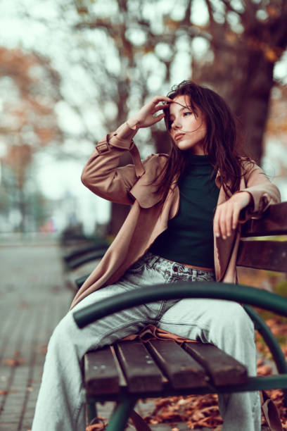 istock Female Pushing Hair Away Messed Up By Wind While Relaxing On Park Bench 1352663936