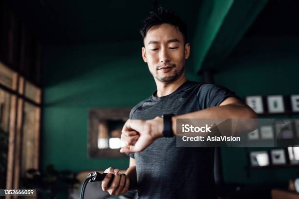 Active Young Asian Man Exercising At Home Using Fitness Tracker App On Smartwatch To Monitor Training Progress And Measuring Pulse Keeping Fit And Staying Healthy Health Fitness And Technology Concept Stock Photo - Download Image Now