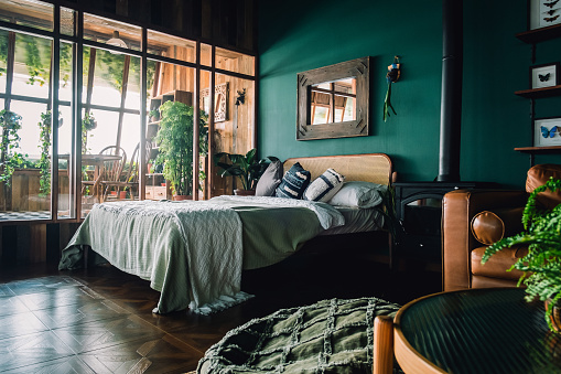 A stylish loft bedroom interior with brown coloured rattan furniture and wooden elements with dark green coloured wall. Decorated with plants