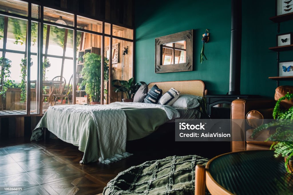 A stylish loft bedroom interior with brown coloured rattan furniture and wooden elements with dark green coloured wall. Decorated with plants Bedroom Stock Photo