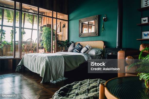 A Stylish Loft Bedroom Interior With Brown Coloured Rattan Furniture And Wooden Elements With Dark Green Coloured Wall Decorated With Plants Stock Photo - Download Image Now