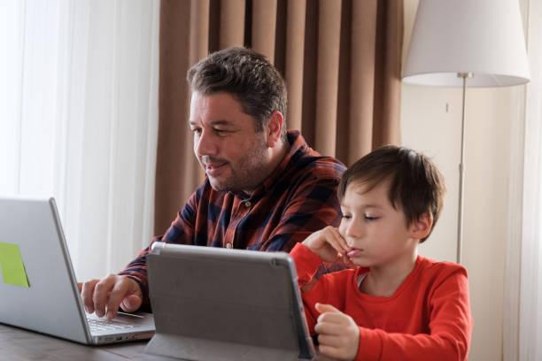 istock Father and child together at home, using digital tablet and laptop 1352666191