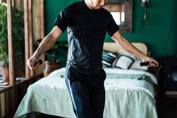 istock Active young Asian man exercising at home, doing rope skipping home workout. Keeping fit and staying healthy. Health and fitness concept 1352666378