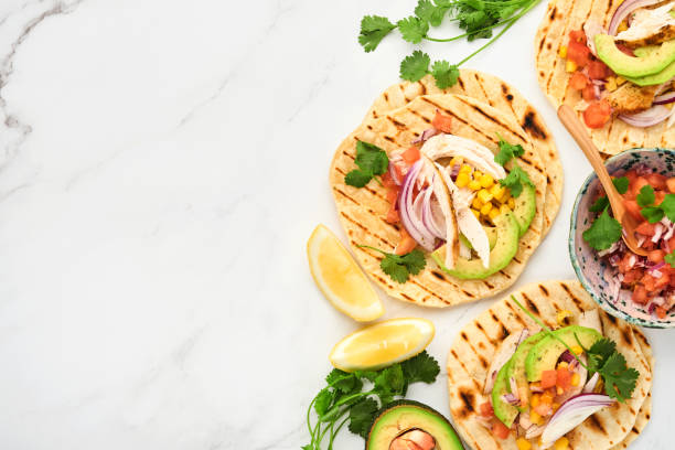 istock Mexican tacos with grilled chicken, avocado, corn kernels, tomato, onion, cilantro and salsa at white stone table. Traditional Mexican and Latin american street food. Top view. 1352666589