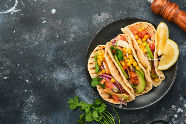 istock Mexican tacos with grilled chicken, avocado, corn kernels, tomato, onion, cilantro and salsa at black stone table. Traditional Mexican and Latin american street food. Top view. 1352666688