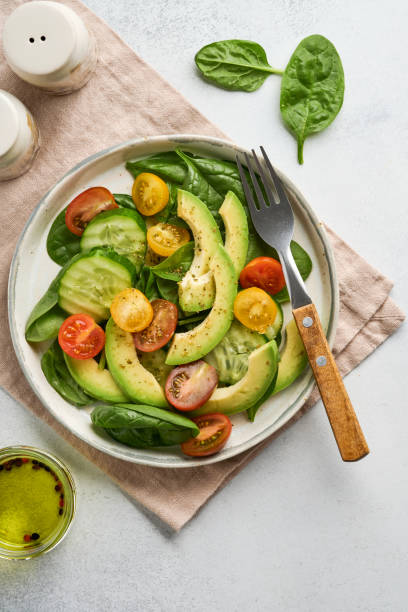 Avocado, red, yellow, black cherry tomato, spinach and cucumber fresh salad with spices pepper and olive oil in grey bowl on grey slate, stone or concrete background. Healthy food concept. Top view. stock photo