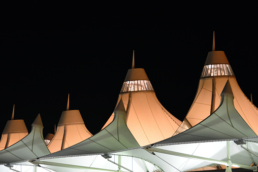 Denver, Colorado, USA: main terminal (Elrey B Jeppesen terminal) at night - glowing tensile fiberglass roof at night, inspired in the snow-capped Rocky Mountains and Native American teepee - designed by Curtis W. Fentress, of Fentress Bradburn Architects Denver International Airport.