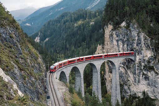 view from above on Landwasserviadukt railroad bridge in Switzerland with red train passing