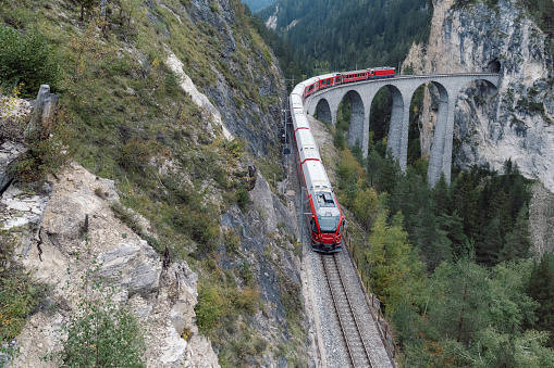 view from above on Landwasserviadukt railroad bridge in Switzerland with red train passing