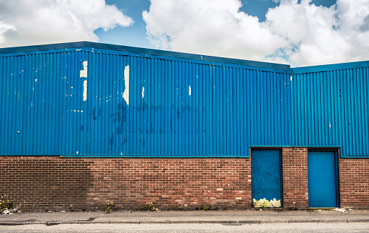 The exterior of a heavily weathered industrial warehouse building on a street in an old industrial estate.