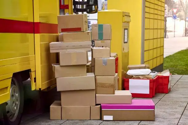 Stack of parcels next to a delivery van are standing on the sidewalk.