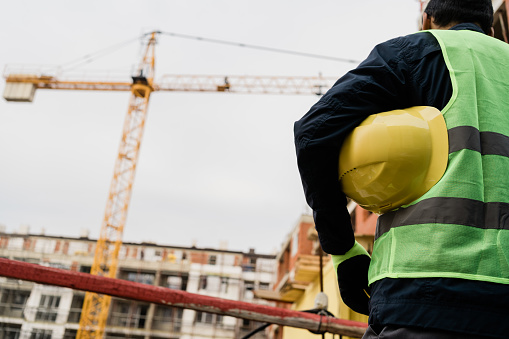 Rear view of construction worker holding helmet at construction site.