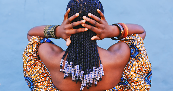 Foto retrovisor de una mujer joven vestida con ropa tradicional africana y sintiendo su cabello sobre un fondo azul photo