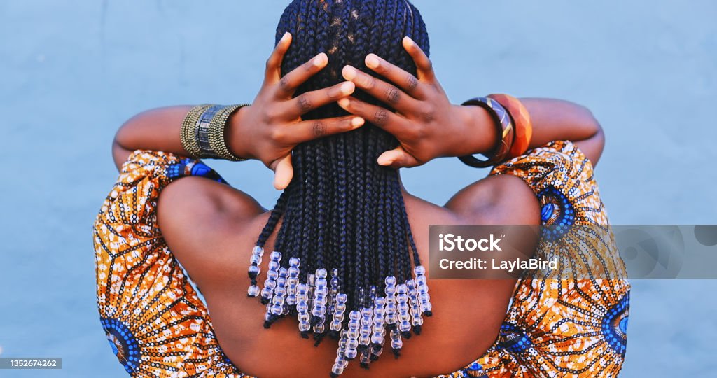 Rearview shot of a young woman wearing traditional African clothing and feeling her hair against a blue background Cornrows fit for a queen African Ethnicity Stock Photo