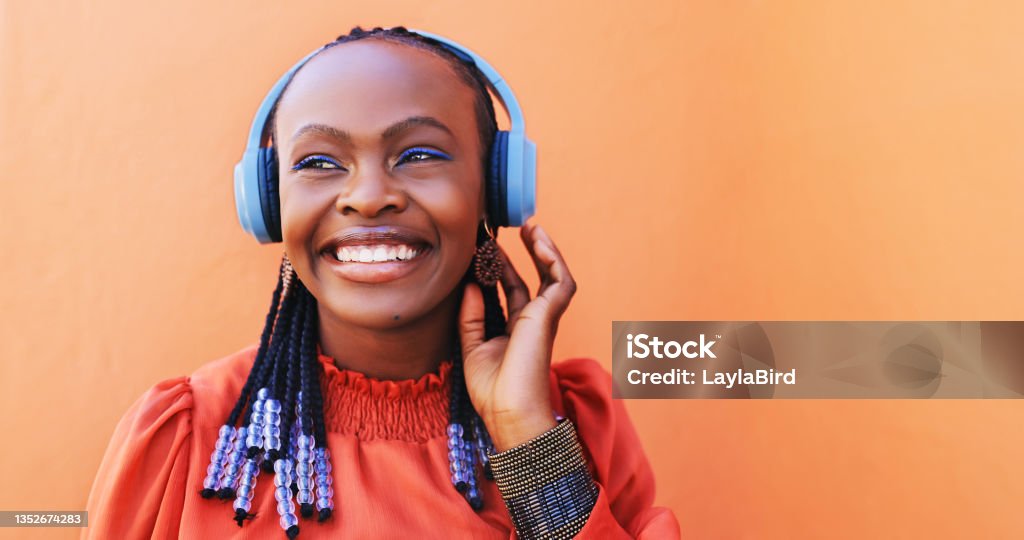 Shot of a beautiful young woman using headphones against an orange background Good tunes, good mood Podcasting Stock Photo