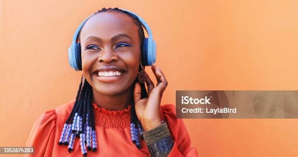 Shot Of A Beautiful Young Woman Using Headphones Against An Orange Background Stock Photo - Download Image Now