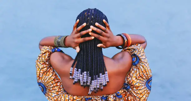 Photo of Rearview shot of a young woman wearing traditional African clothing and feeling her hair against a blue background