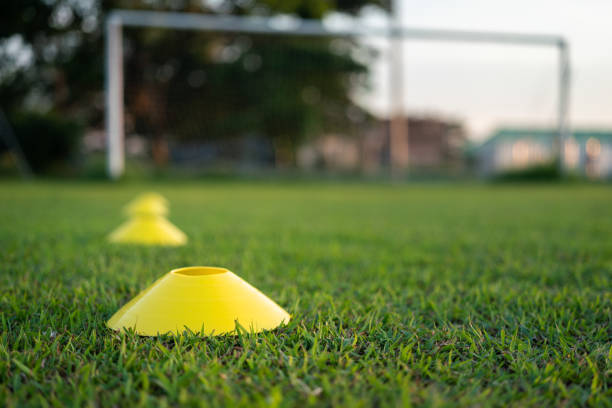 Football training cone for speed and moving practice is placed on firm ground pitch. Sport equipment object - challenge activity scene photo. Selective focus at the front cone.