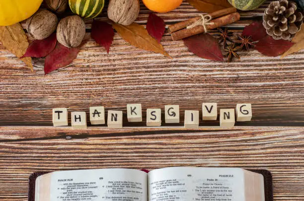 Thanksgiving word on wooden cubes with handwritten letters, open Holy Bible Book, and fall fruits on wooden table. A Christian thanksgiving concept. Top view. Giving thanks to God Jesus Christ.