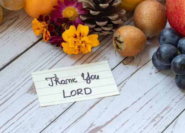 A handwritten note: Thank you, LORD, with fall fruits on wooden background. A biblical concept of Christian thanksgiving and gratitude to God Jesus Christ. A close-up of autumn food.