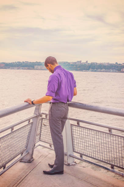 istock Young man standing outdoors by river in New York City, looking down, thinking 1352682198