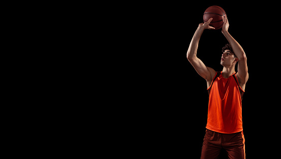 For three. Studio shot of young man, basketball player doing set shot isolated on dark background. Sport, energy, power, results. Motion, activity, movement concepts. Flyer with copy space for ad