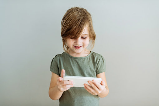 five year old girl using smart phone, studio shot on grey