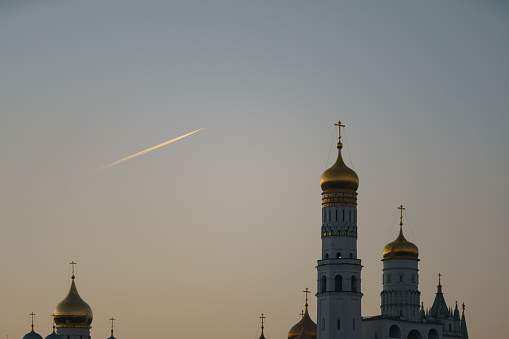 Moscow downtown. Kremlin Tower,  Ivan the Great Bell Tower, Dormition Cathedral. Beautiful view. Landmark in capital of the Russian Federation during sunset. White contrail of an airplane in the sky