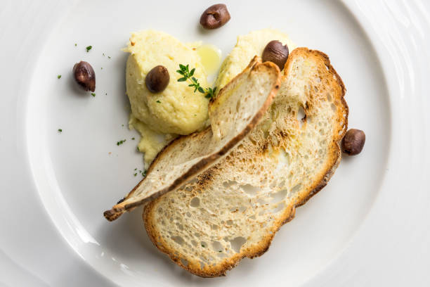Plate of Ligurian-style cod fish with crispy bread and olives on white background