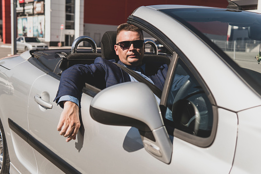 Stylish man sitting in sport car. A successful businessman rides an expensive convertible car around the city during the day.