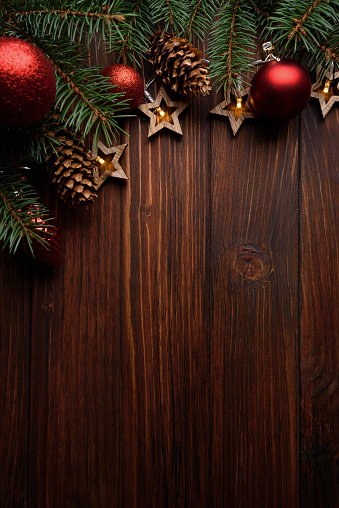 Christmas background with fir branches, cones, red baubles and star shape lights on dark wooden board. Top view. Copy space. Xmas decoration