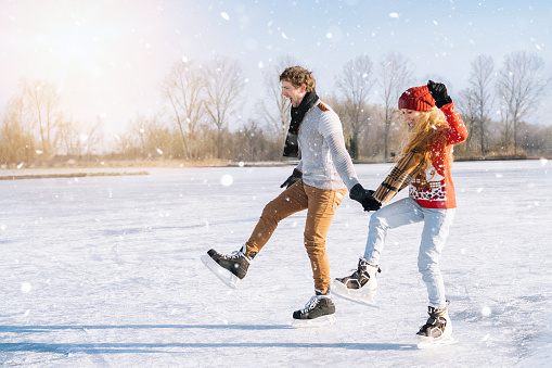 Loving couple in warm sweaters having fun on ice. Woman and man ice skating outdoors in sunny snowy day. Active date on ice arena in winter Christmas Eve. Romantic activities and lifestyle concept