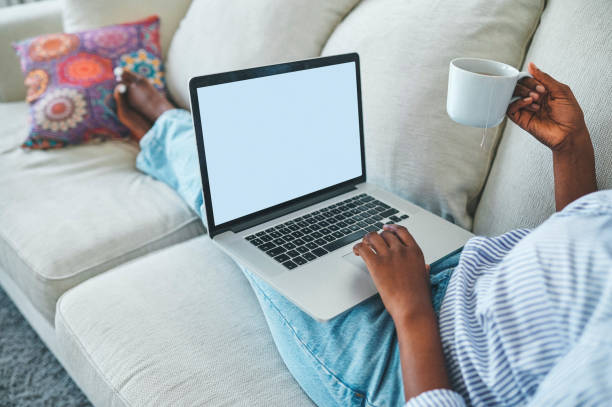 istock Closeup shot of an unrecognisable woman drinking tea and using a laptop while relaxing on a sofa at home 1352697885