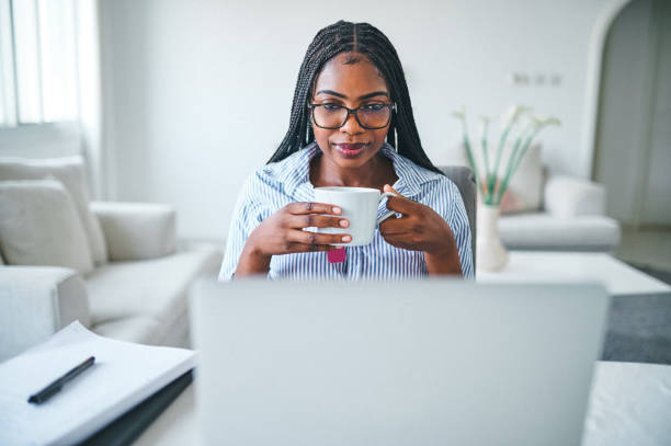 istock Shot of a young woman drinking tea while using a laptop at home 1352697889