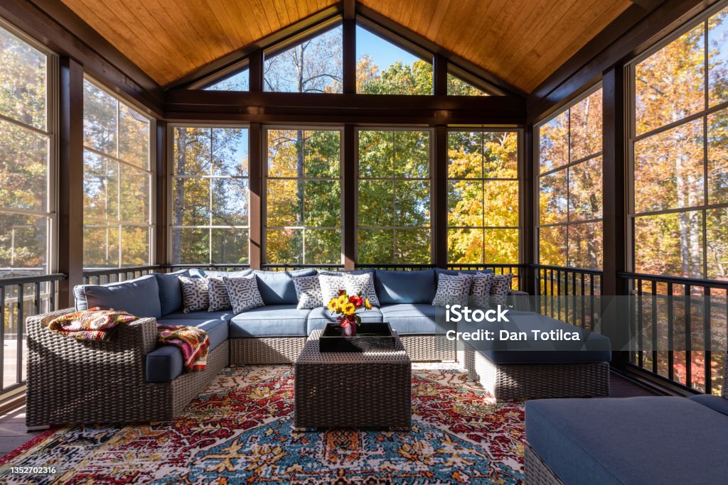 Cozy Furnished Porch Enclosure in Autumn Season Cozy screened porch with contemporary furniture and flower bouquet in a vase, autumn leaves and woods in the background. Autumn Stock Photo