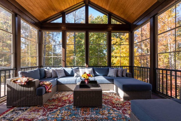 Cozy Furnished Porch Enclosure in Autumn Season Cozy screened porch with contemporary furniture and flower bouquet in a vase, autumn leaves and woods in the background. porch stock pictures, royalty-free photos & images
