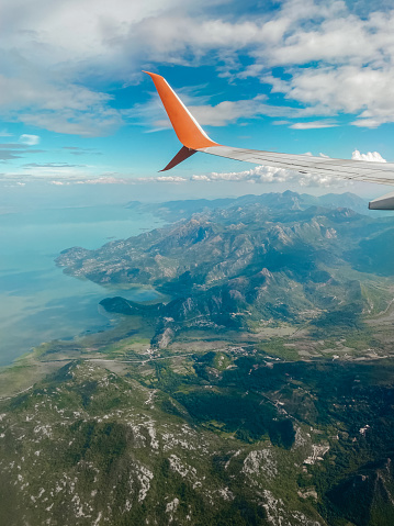 A gorgeous view from the porthole is a beautiful picturesque photo of an airplane wing against the backdrop of the green mountains of Montenegro.