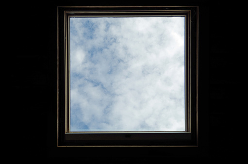 Skylight surrounded by darkness. Blue sky and clouds. Conceptual metaphor.