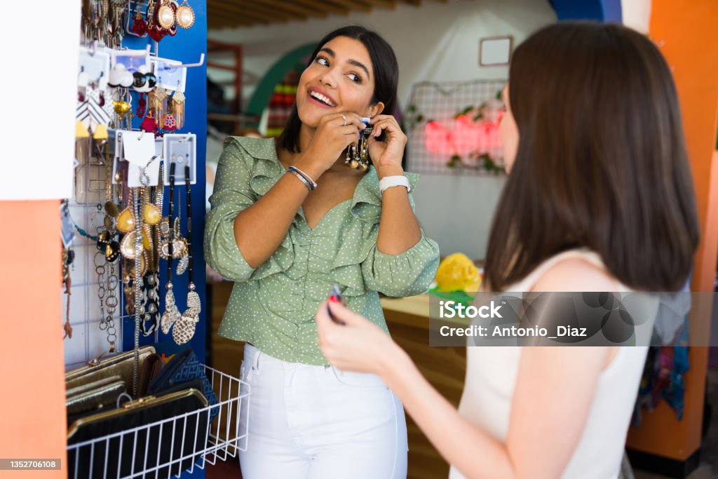Best friends going shopping together Attractive young woman and her friend trying on a pair of beautiful earrings at the thrift store Jewelry Stock Photo