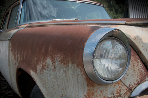 Partial view of the front and right side of an old rusted American car with headlight