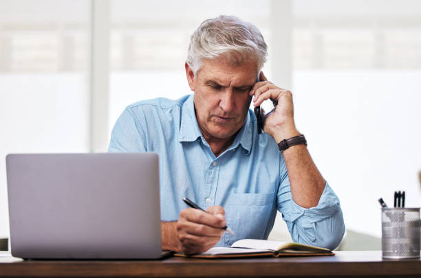 istock Shot of a mature man making notes while talking on his cellphone 1352715402