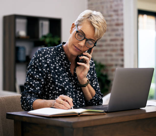 istock Shot of a mature woman making notes while talking on her cellphone 1352715409