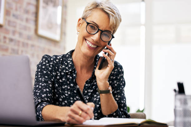 istock Shot of a mature woman making notes while talking on her cellphone 1352715410