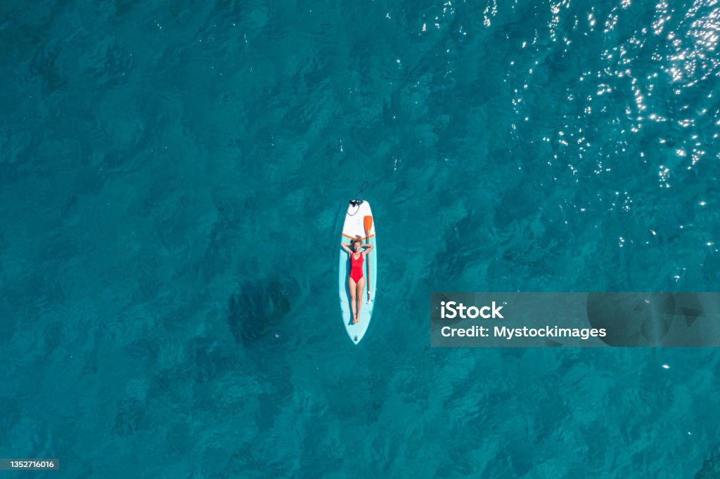 Aerial view of woman floating on a stand up paddle She lies down on a  paddle board and enjoys relaxation on tropical turquoise lagoon Beach Stock Photo
