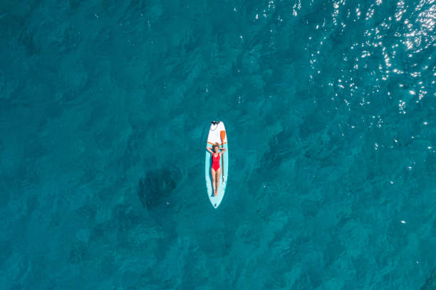 Aerial view of woman floating on a stand up paddle She lies down on a  paddle board and enjoys relaxation on tropical turquoise lagoon paddleboard photos stock pictures, royalty-free photos & images