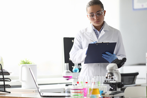 Woman scientist chemist writing in documents in chemical laboratory. Quality control of petroleum products concept