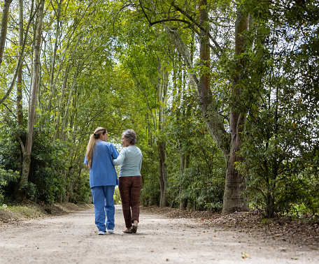 Happy Latin American nurse walking outdoors with a senior woman at a retirement community â assisted living concepts