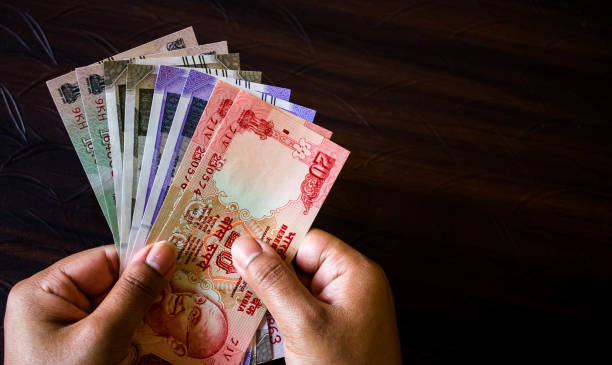 istock Woman's hand holding Indian currency on working desk isolated on a dark background 1352722848