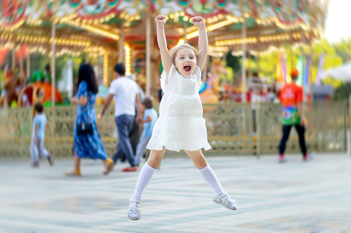 baby girl jumps and smiles with happiness in an amusement park in the summer